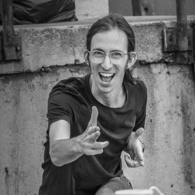 Greg Edelston, kneeling with a big grin and finger-guns