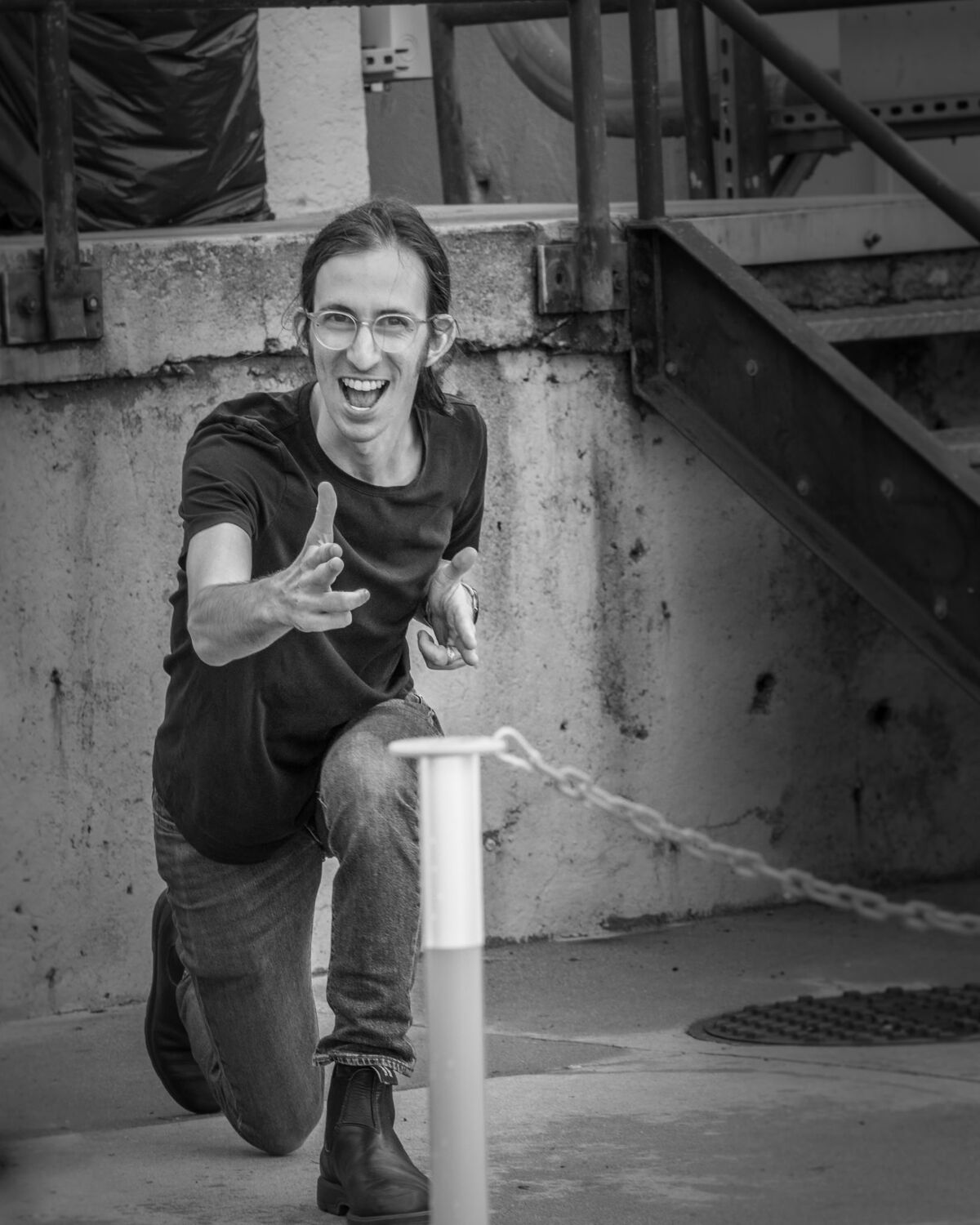 Greg Edelston kneeling on a sidewalk, grinning, pointing finger-guns at the camera